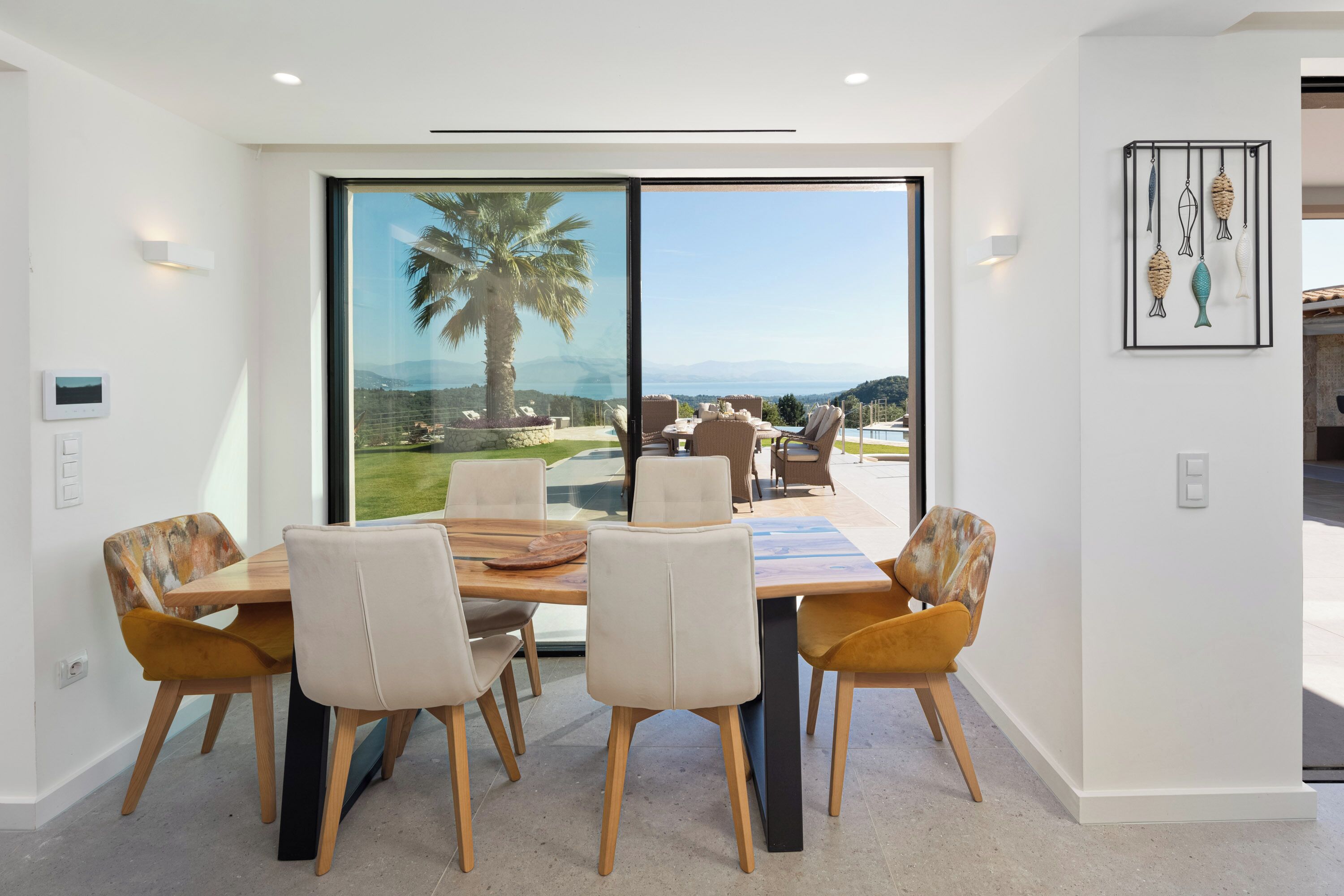 Un comedor con una mesa grande y sillas, vistas al exterior y una obra de arte colgada en la pared.