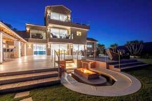 Une maison moderne à deux étages, dotée d’une vaste terrasse extérieure, d’un foyer et d’une entrée bien éclairée.