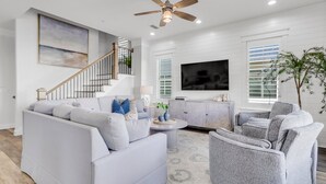 A modern living room with a grey sofa, a grey armchair, a round coffee table, and a ceiling fan. - Flash Sale! Charming home in Orange Beach, AL (Orange Beach)