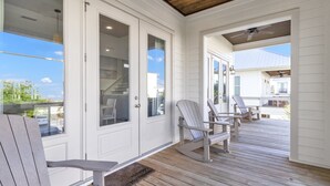 A covered porch with wooden chairs and a view of the outside. - Flash Sale! Charming home in Orange Beach, AL (Orange Beach)
