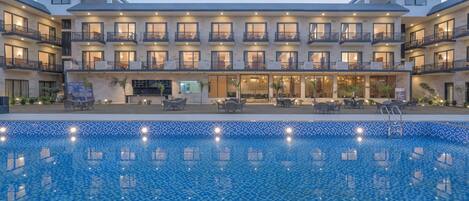 A hotel with a swimming pool, outdoor seating, and multiple balconies.