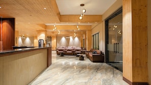 A spacious lobby with a wooden reception desk, plush seating area, and a marble floor. - Vanashraya corbett (Kaladhungi)