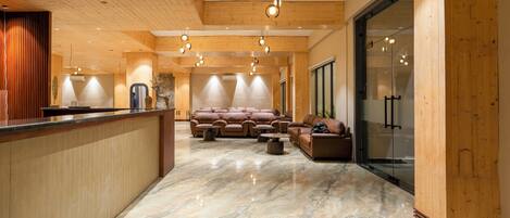 A spacious lobby with a wooden reception desk, plush seating area, and a marble floor.