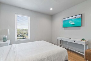A bedroom with a bed, a window with blinds, a television on the wall, and a white console table.