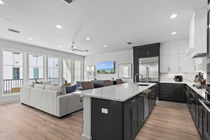 A modern kitchen with dark cabinetry, a marble island, and a large window overlooking a balcony.