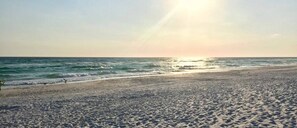 Una spiaggia con sabbia e acqua, un cielo sereno e il sole all'orizzonte.