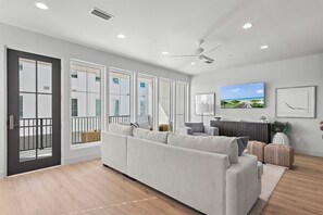 Un salon moderne avec un grand canapé, un téléviseur à écran plat et un ventilateur de plafond.