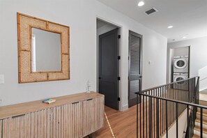 Un couloir avec une console en bois, un miroir, une porte et un coin buanderie équipé d’un lave-linge.