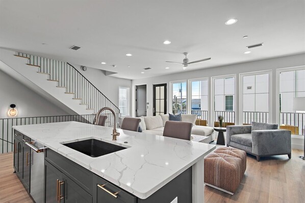 A modern kitchen with a marble island, a built-in sink, and a staircase leading to another level.