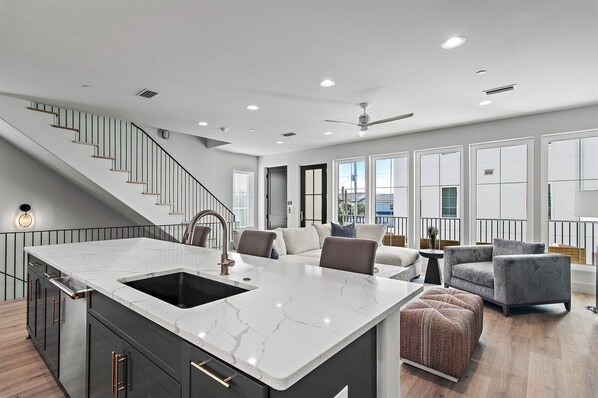 A modern kitchen with a marble island, a built-in sink, and a staircase leading to an upper level.