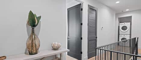 En modern inredning med en vit vägg, en vas med en växt, en liten skål, en dörr och en tvättstuga med en tvättmaskin.