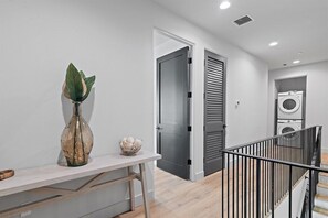 A modern interior with a white wall, a vase with a plant, a small bowl, a door, and a laundry area with a washing machine.