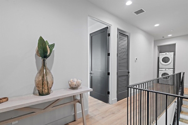 A modern interior with a white wall, a vase with a plant, a small bowl, a door, and a laundry area with a washing machine.