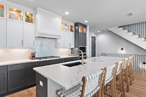 Una cucina moderna con isola in marmo, mobili scuri e una scala che conduce a un piano superiore.