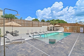 A pool area with lounge chairs, umbrellas, and a wooden fence.