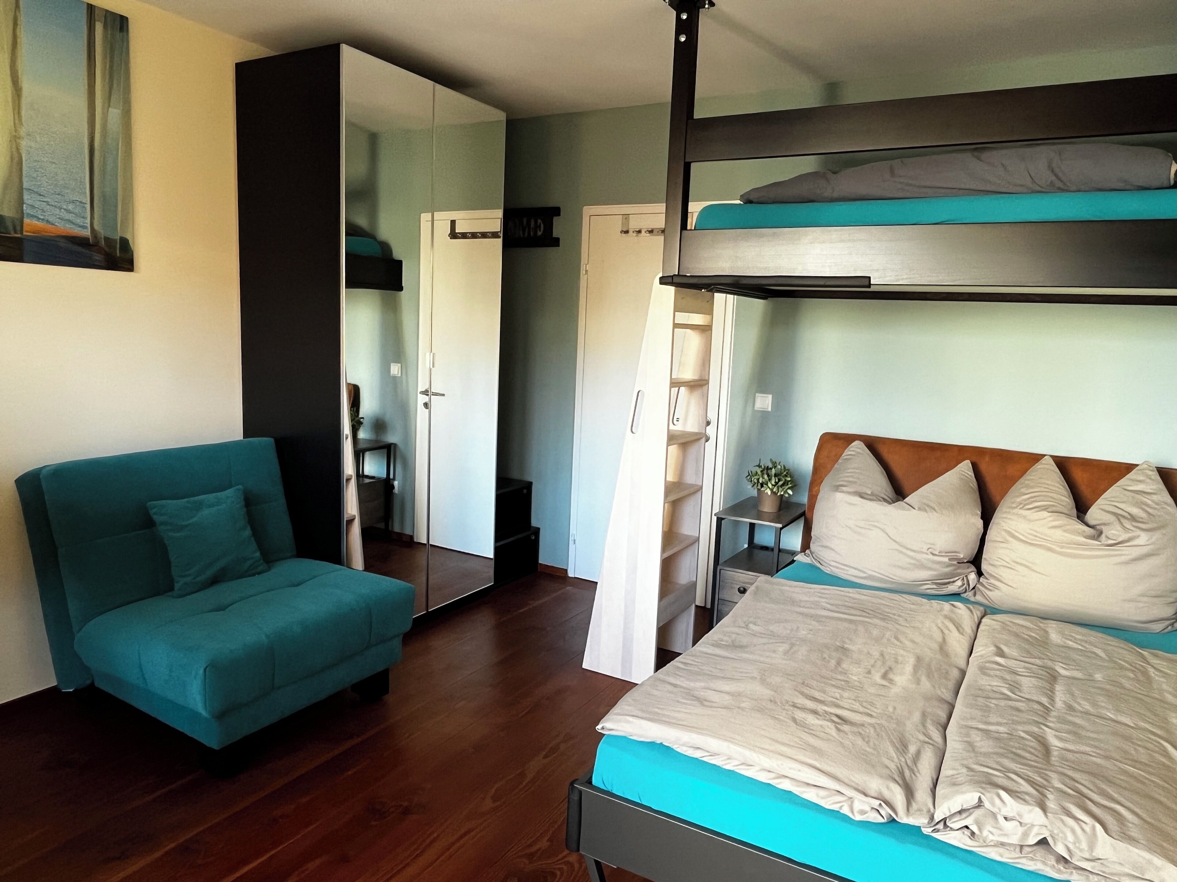 Une chambre avec un lit superposé, un canapé de couleur turquoise et un plancher en bois.