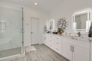 Une salle de bain moderne avec une douche à parois de verre, des meubles blancs et un pare-baignoire en marbre.