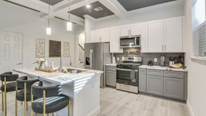 A modern kitchen with white cabinets, stainless steel appliances, and a central island with bar stools. - 4 Mi to NRG Stadium: Luxurious Houston Townhome! (Houston)