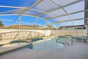 A covered swimming pool with a hot tub, lounge chairs, and a view of the surrounding area.