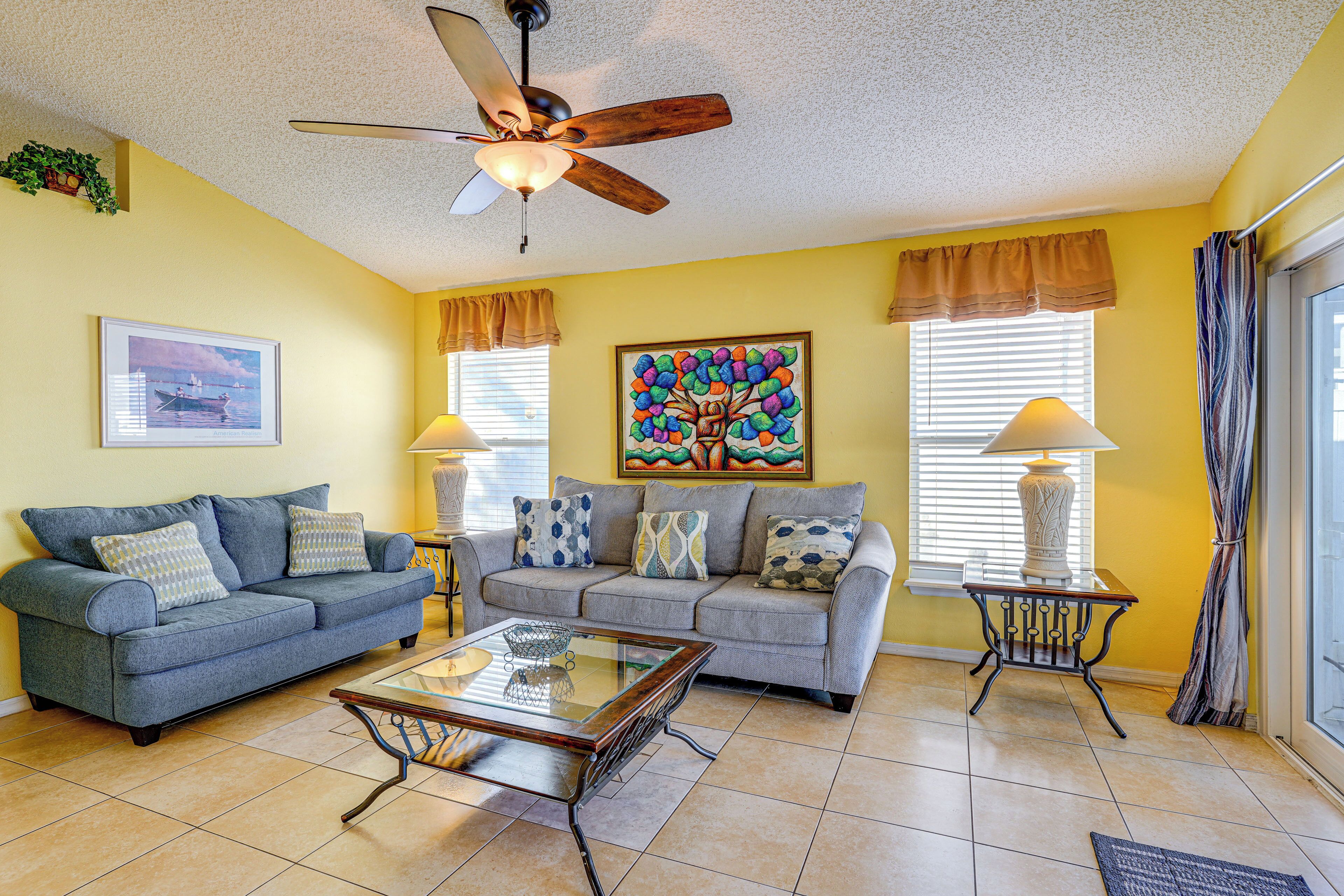 A living room with two sofas, a coffee table, a ceiling fan, and a painting on the wall.