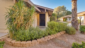 A residential building with a brick facade, a black door, and a landscaped garden with various plants and a palm tree. - Golf, Hike, Swim: Your Perfect Desert Oasis Escape (Mesa)