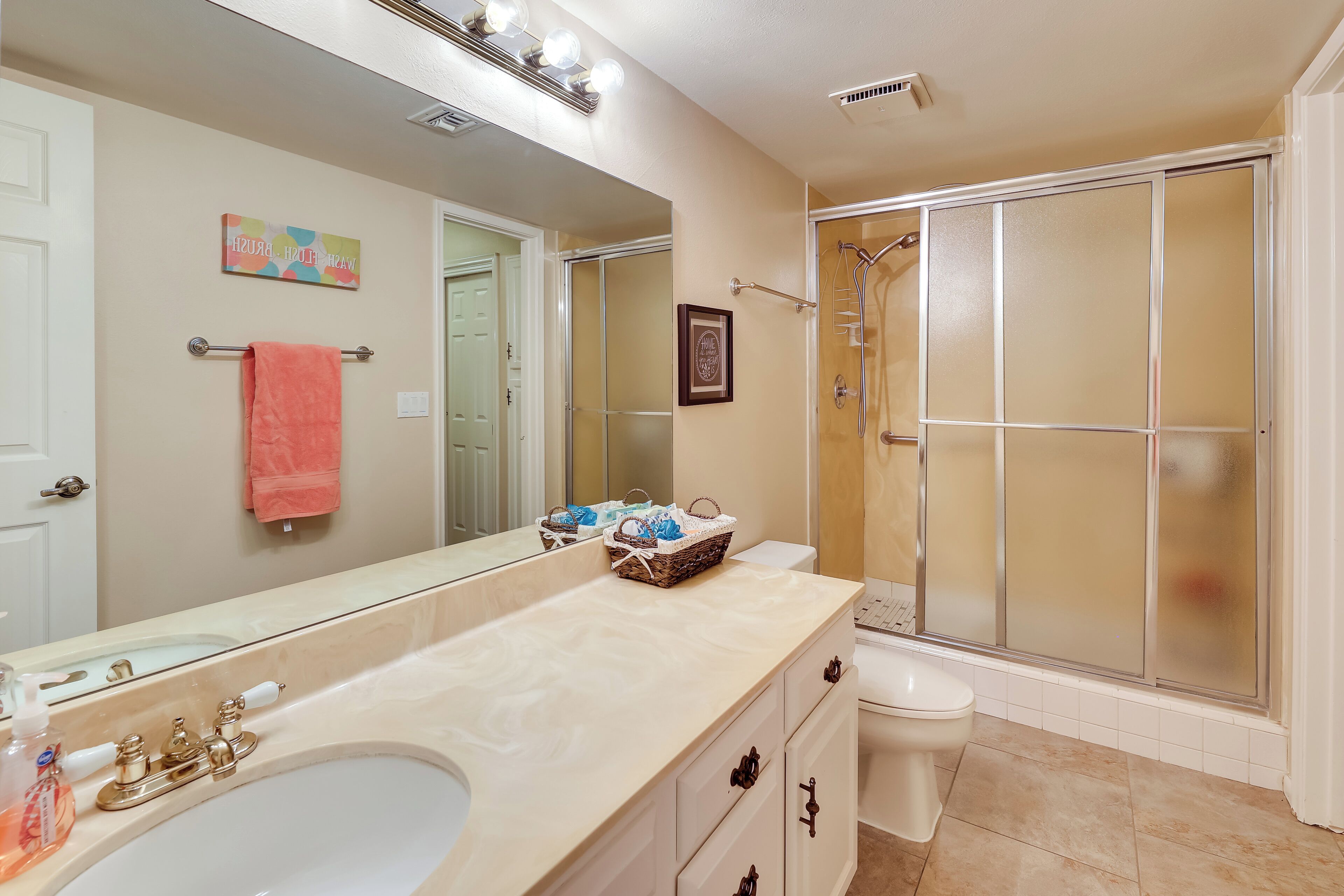A bathroom with a large mirror, a sink with a faucet, a toilet, and a shower enclosure.