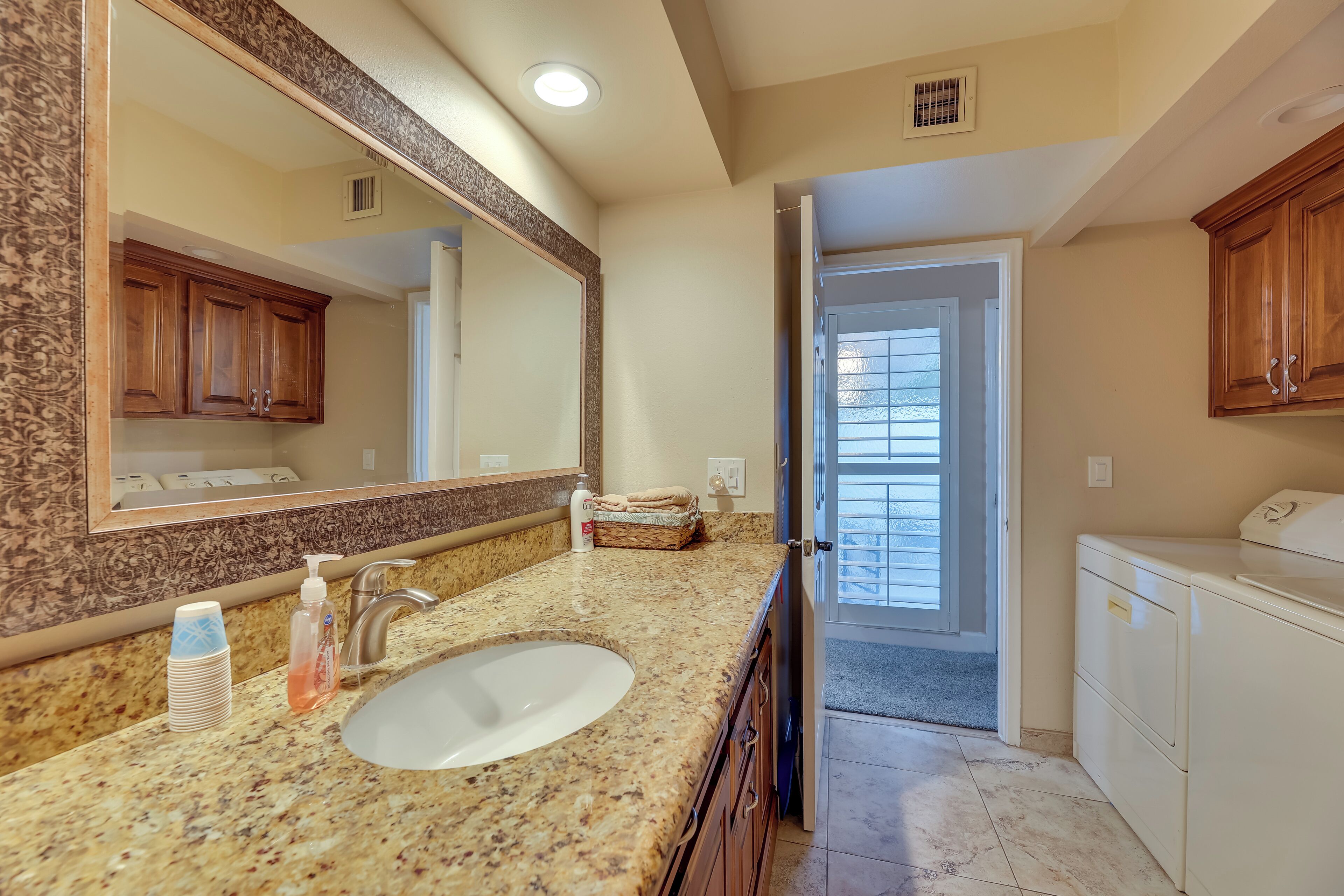 A bathroom with a granite countertop, a large mirror, wooden cabinets, and a white sink.