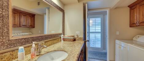 A bathroom with a granite countertop, a large mirror, wooden cabinets, and a white sink.