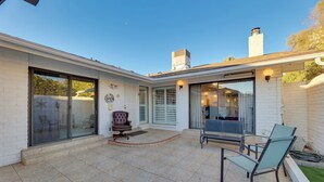 A modern house with a patio area featuring a sliding glass door, a cushioned chair, and a dining table with chairs. - Golf, Hike, Swim: Your Perfect Desert Oasis Escape (Mesa)