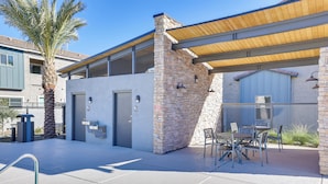 Un edificio moderno con fachada de piedra, un patio cubierto con mesas al aire libre y una palmera.