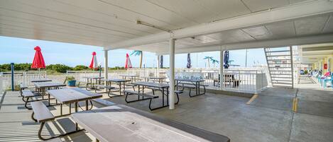 A covered picnic area with benches and tables, a railing, and a view of the beach.