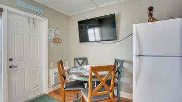 A dining area with a table, chairs, a television, and a refrigerator.