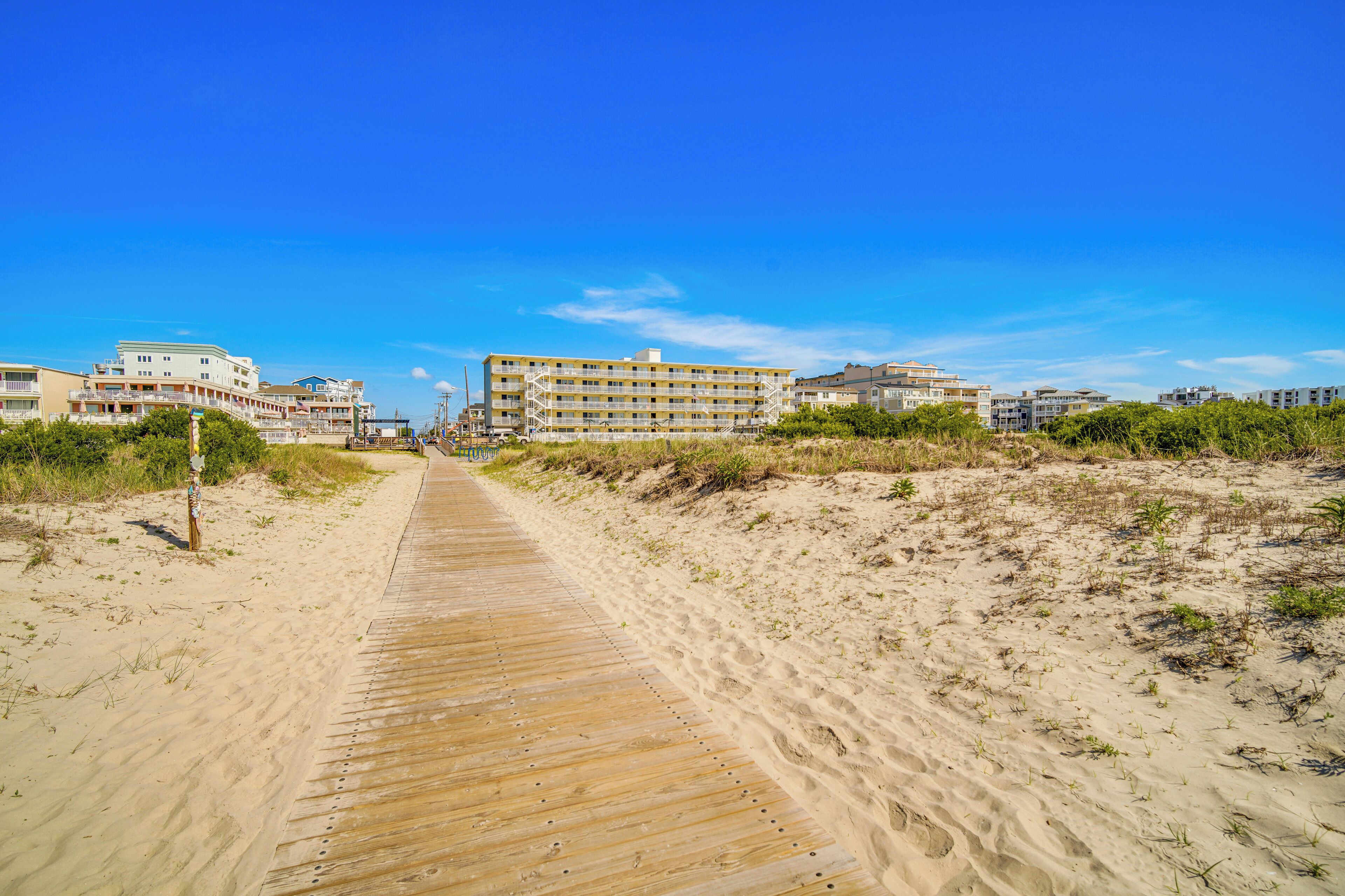 A sandy boardwalk leading to a beachfront hotel with multiple buildings.
