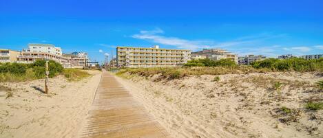 A sandy boardwalk leading to a beachfront hotel with multiple buildings.