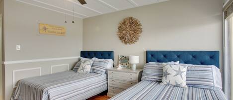 A bedroom with two beds, a ceiling fan, a decorative wall piece, and a sign on the wall.