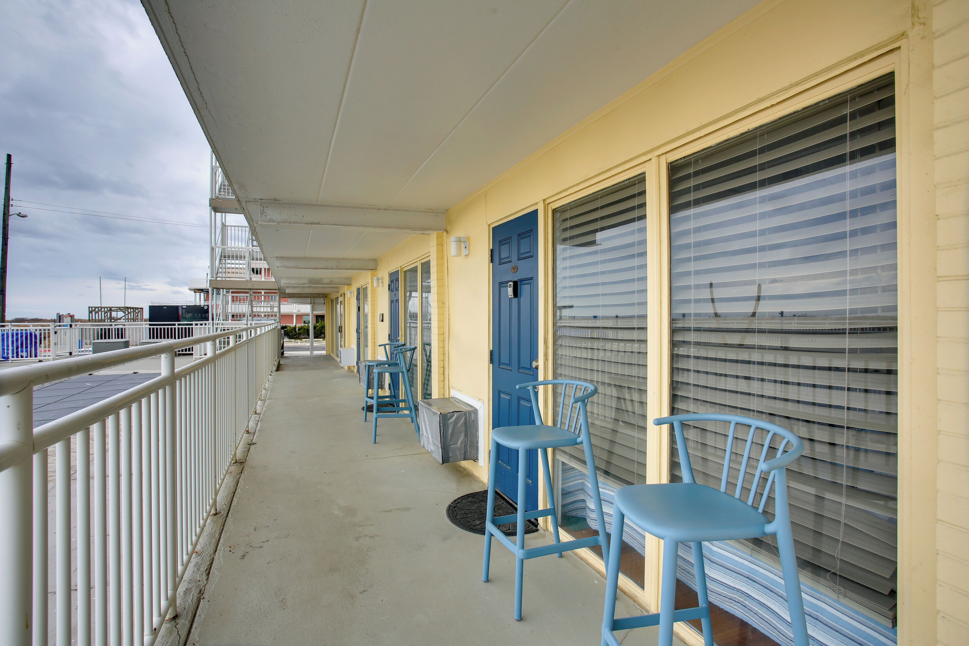 A covered balcony with blue chairs and a blue door, overlooking a dock area.