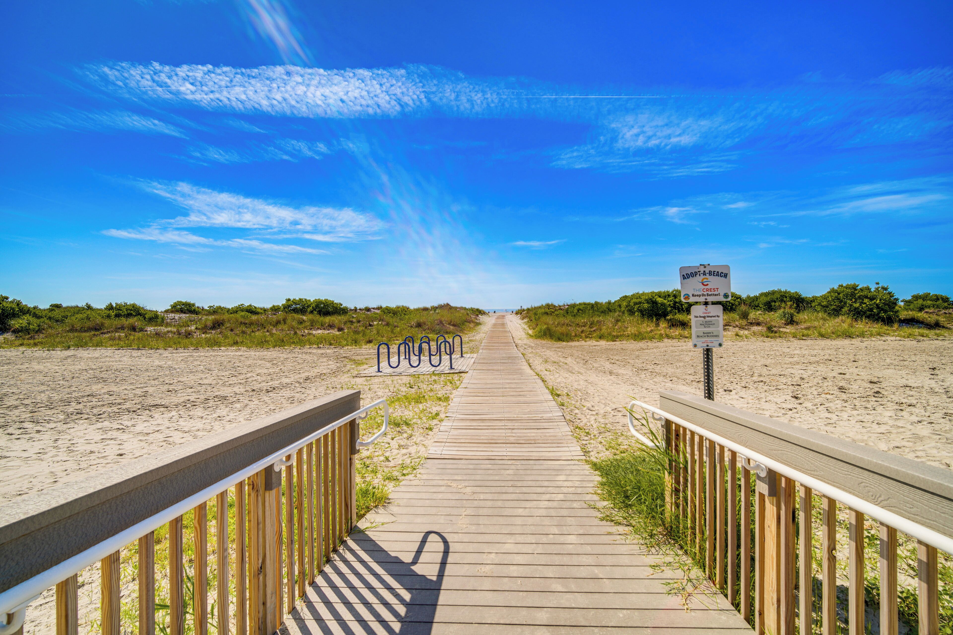 Ein Holzsteg führt zu einem Strand, an dem ein Schild 'Adopt-a-Beach' und das 'Crest'-Logo angebracht sind.