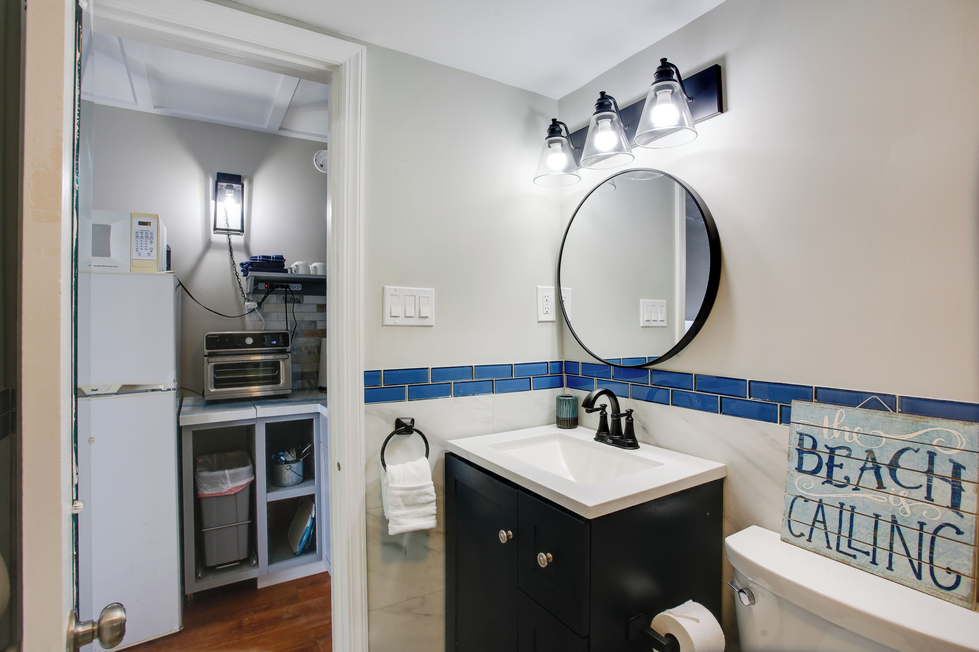 A bathroom with a white sink, black cabinets, a mirror, and a blue-tiled backsplash.