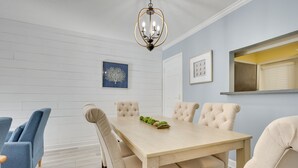 A dining room with a light wooden table, beige upholstered chairs, and a chandelier. - 3 Mi to St Simons Beach: Gem w/ Pool Access & Deck (St. Simons Island)