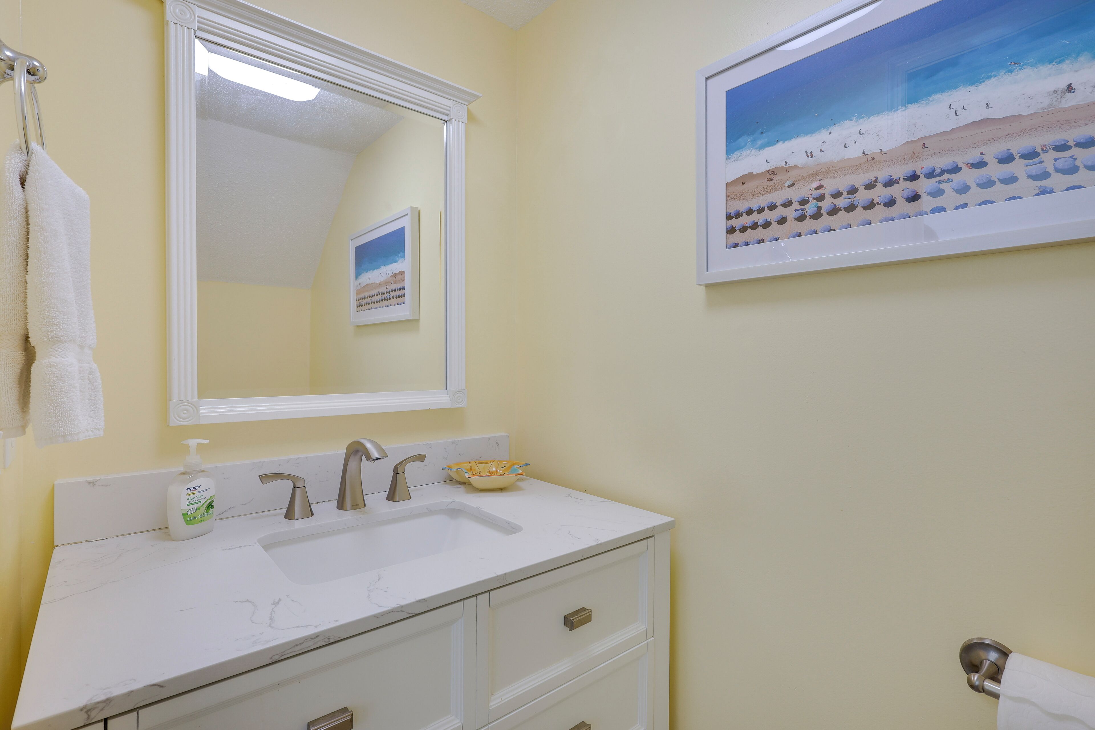 A bathroom with a white sink, a mirror, and a framed beach painting.