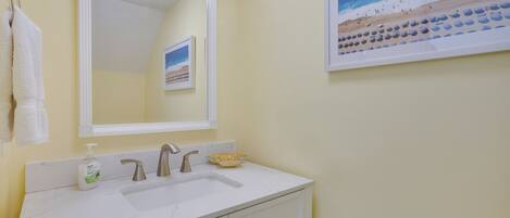 A bathroom with a white sink, a mirror, and a framed beach painting.