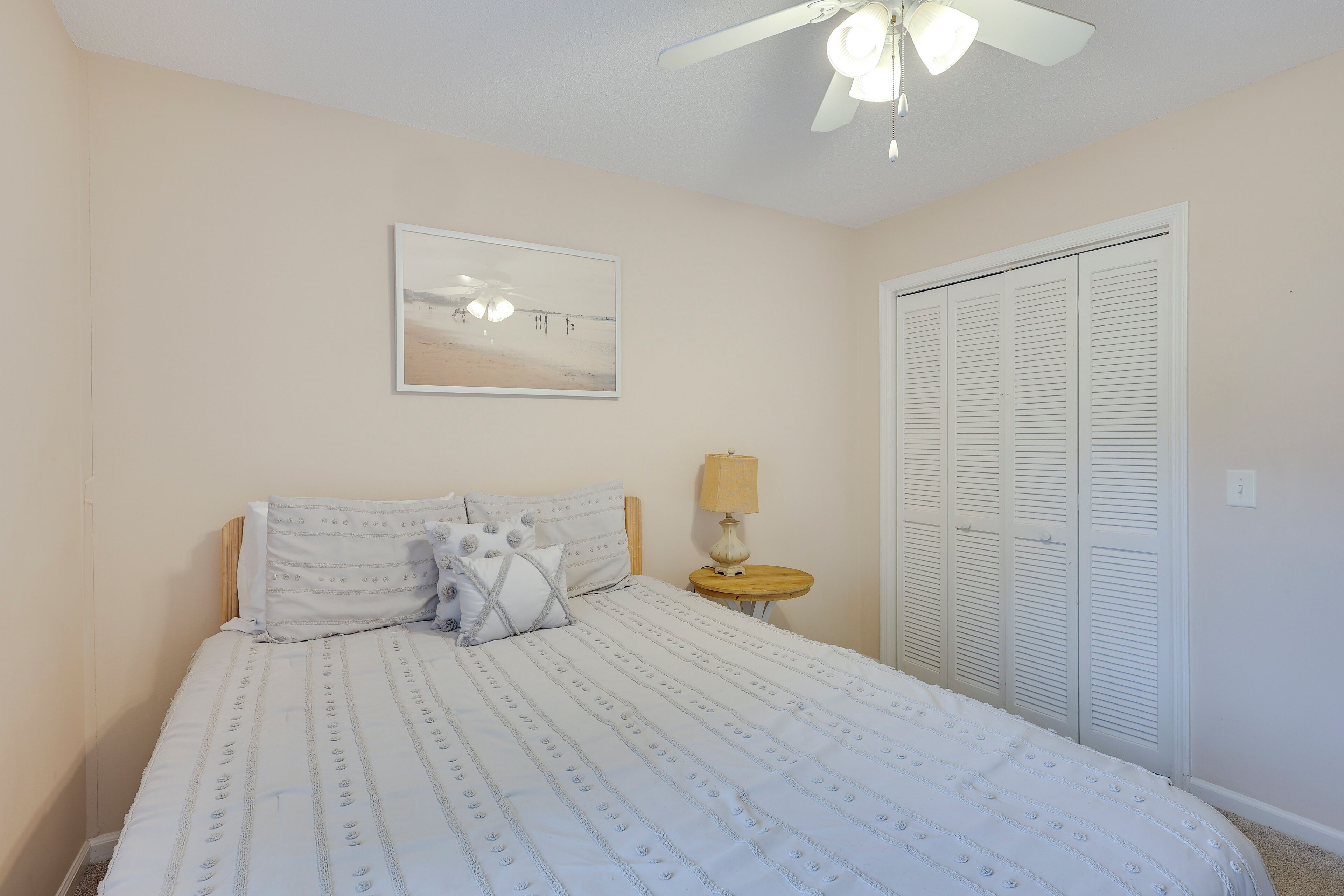 Una camera da letto con un letto, una ventola a soffitto, una lampada da comodino, un armadio e un quadro incorniciato appeso al muro.