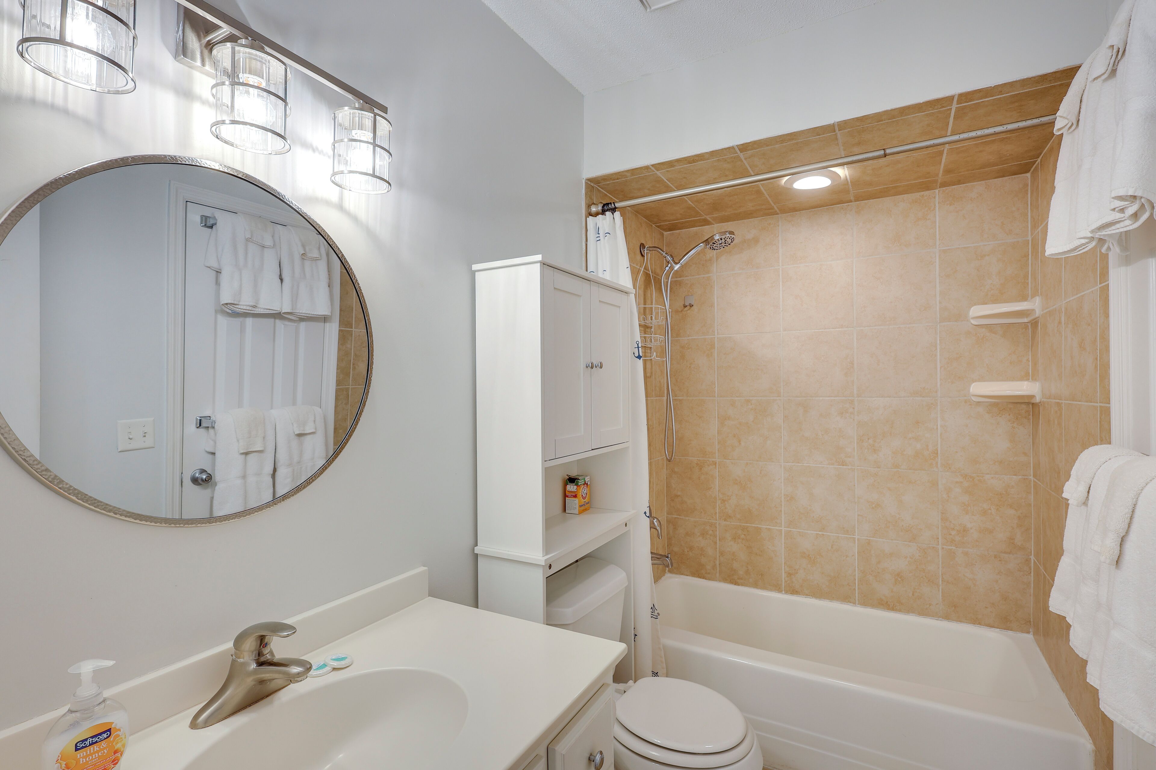 Ein Badezimmer mit einem weißen Waschbecken, einer Toilette, einer Badewanne und einer Dusche. Über dem Waschbecken befindet sich ein Spiegel und über der Badewanne ein Handtuchhalter.