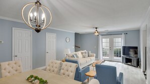A spacious living area with a dining table, blue and white furniture, a chandelier, and a television. - 3 Mi to St Simons Beach: Gem w/ Pool Access & Deck (St. Simons Island)