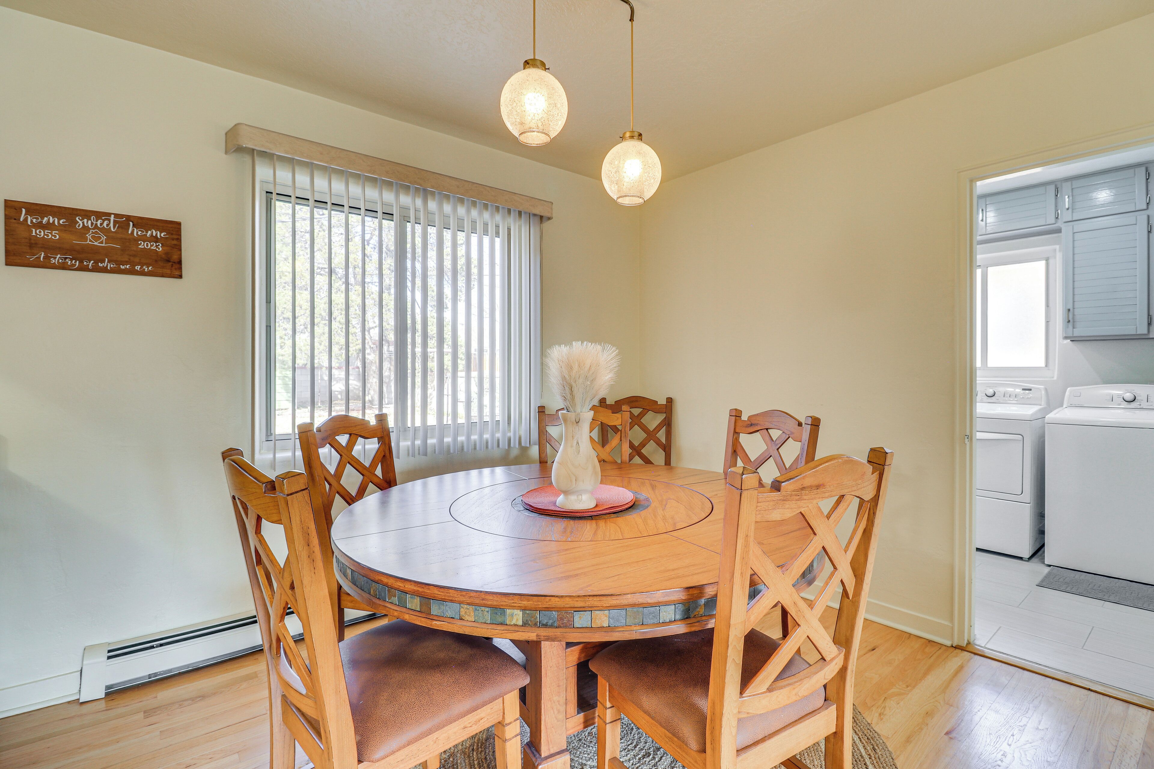 A dining area with a round wooden table, six chairs, a vase, and a sign on the wall.