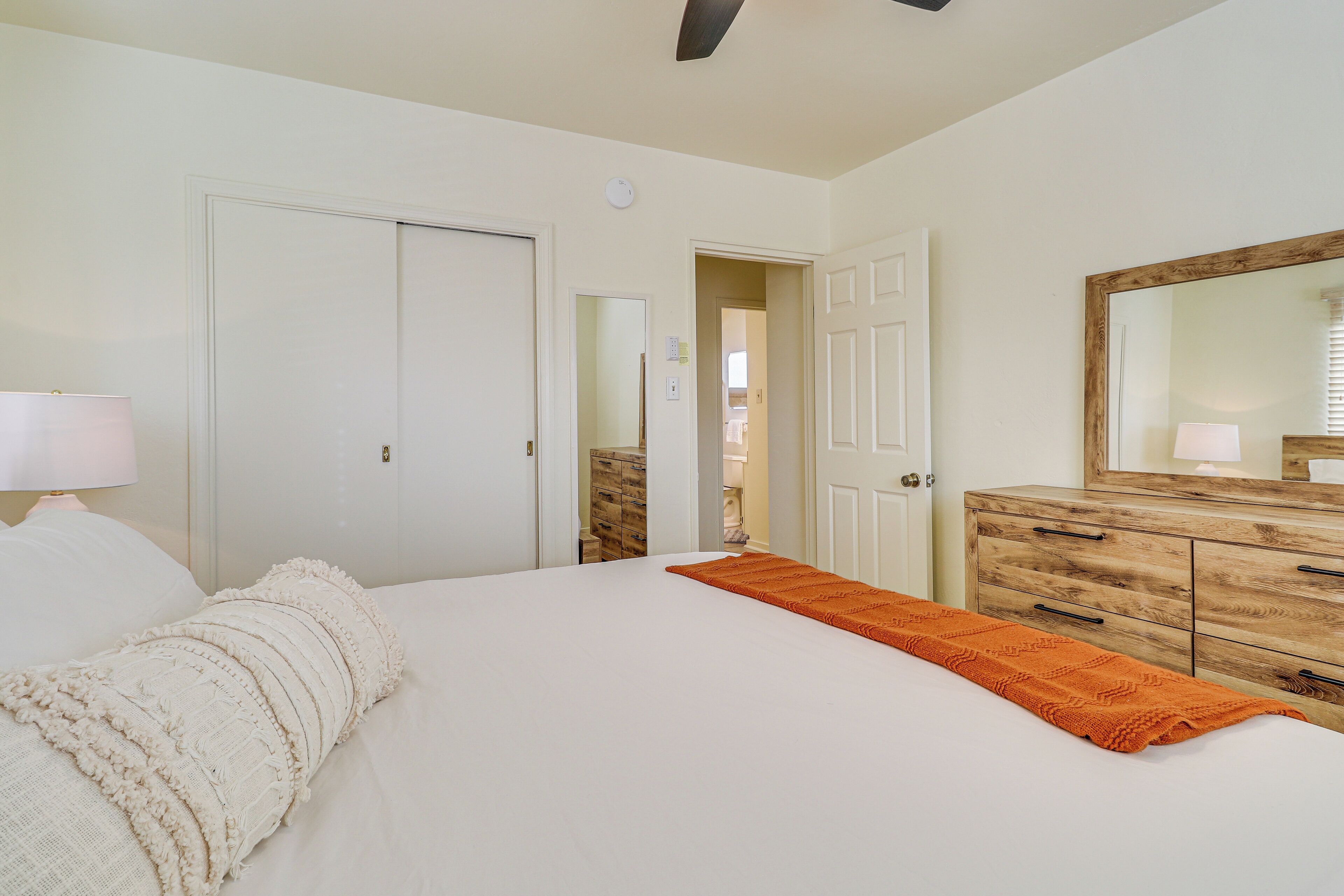 A bedroom with a bed, a dresser, a mirror, and a door leading to another room.
