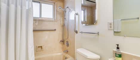 A bathroom with a bathtub, toilet, and a hand sanitizer dispenser.