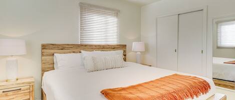 A neatly arranged bedroom with a large bed, wooden headboard, two bedside tables with lamps, a ceiling fan, and a wardrobe.