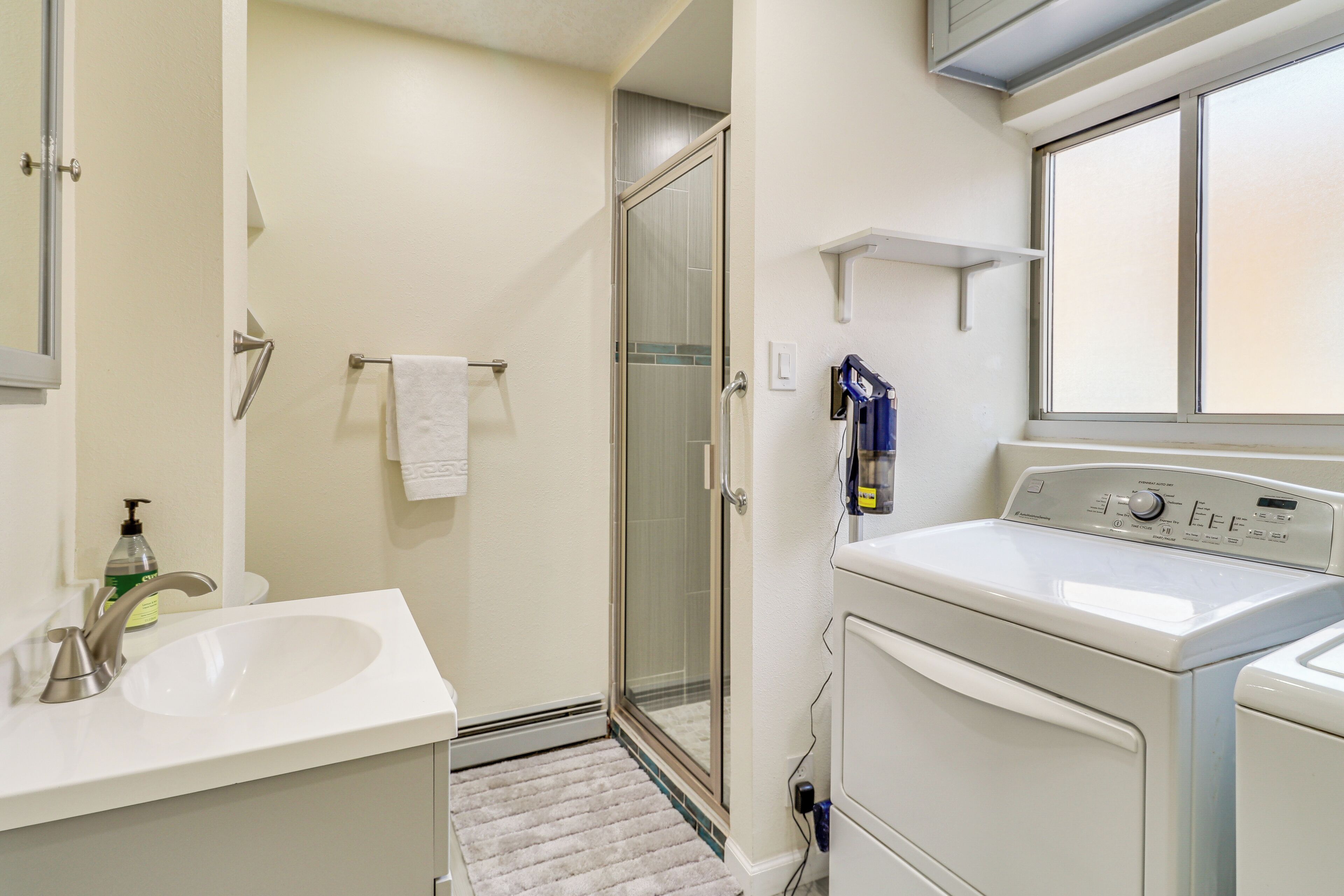 A bathroom with a sink, a glass shower door, and a washing machine.