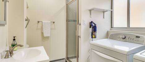 A bathroom with a sink, a glass shower door, and a washing machine.